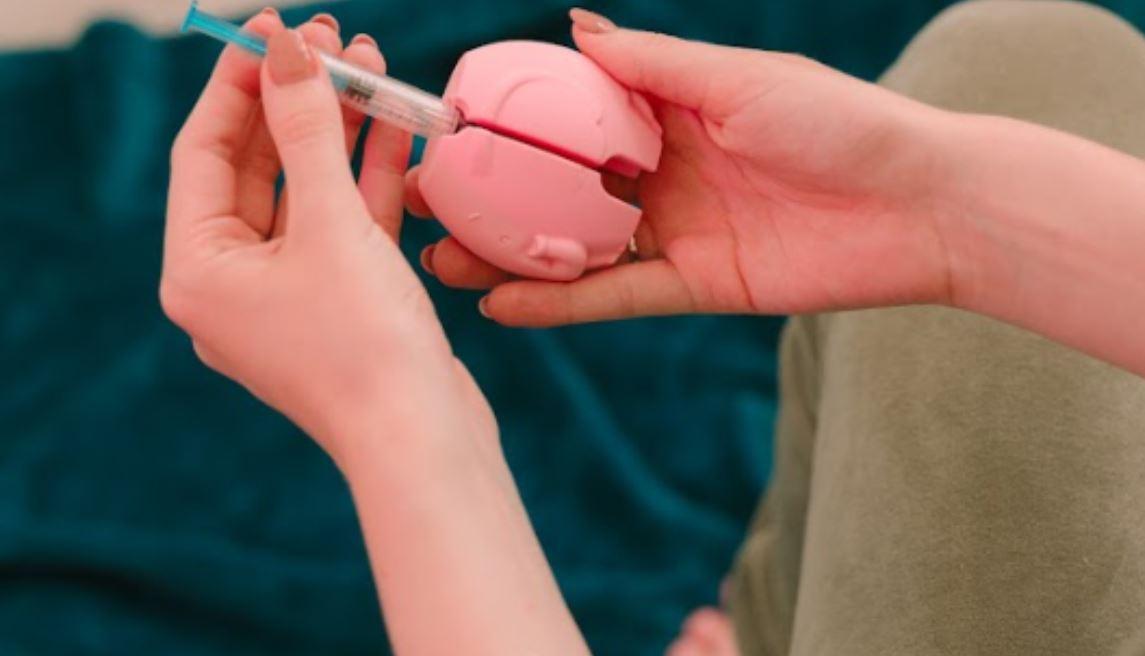 Ženské ruce drží injekci a injekční aplikátor TUGI. Příběhy uživatelů: S TUGI se aplikace injekcí stává snesitelnější